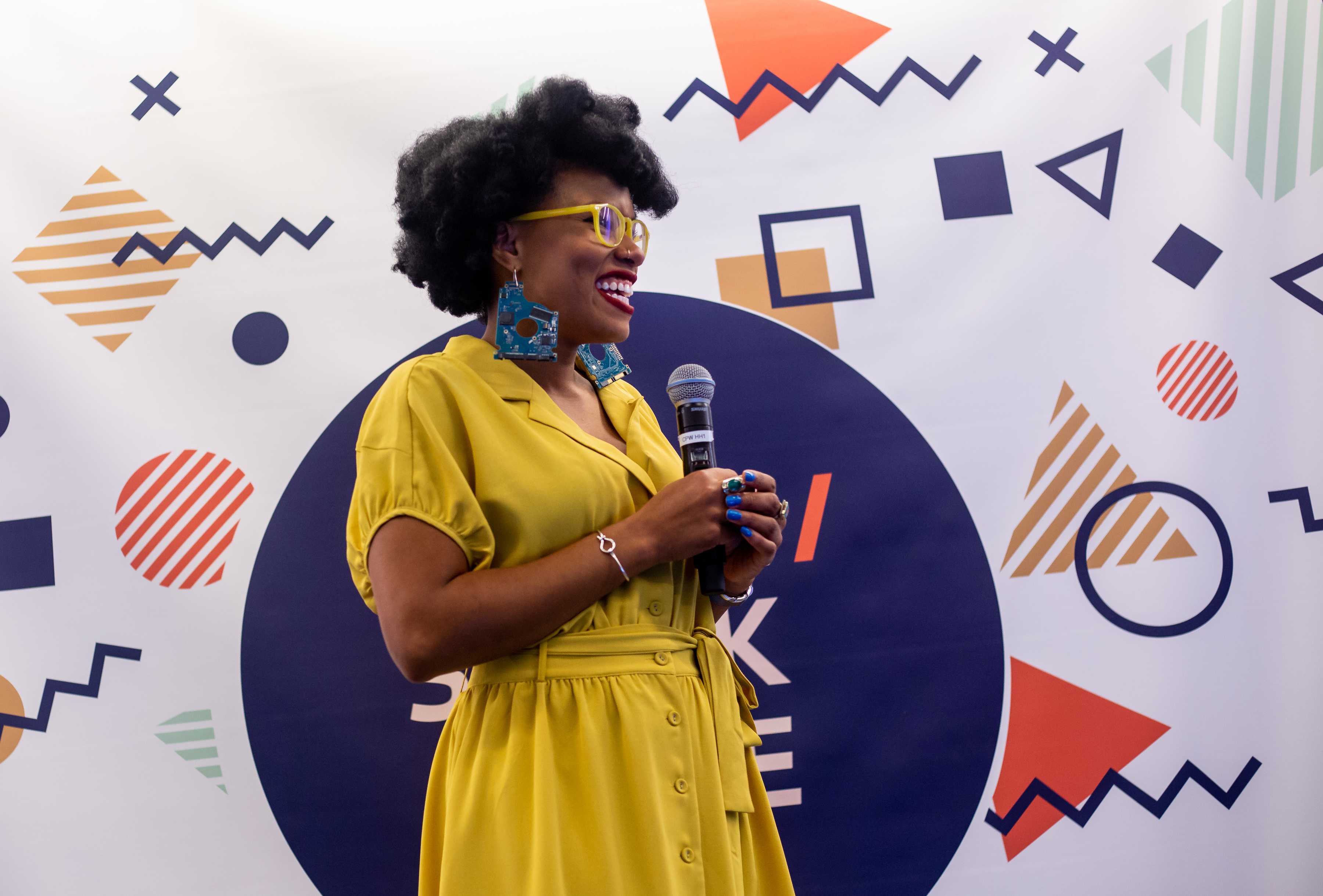 A smiling speaker talks on stage at the 2018 conference with a microphone.